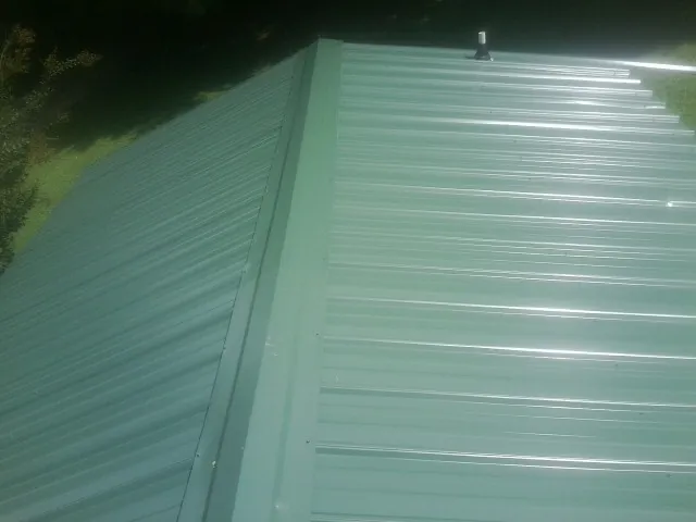 New green metal panels meeting at the ridge of a roof — Flat Roof Repair work by our crew in Lakeville